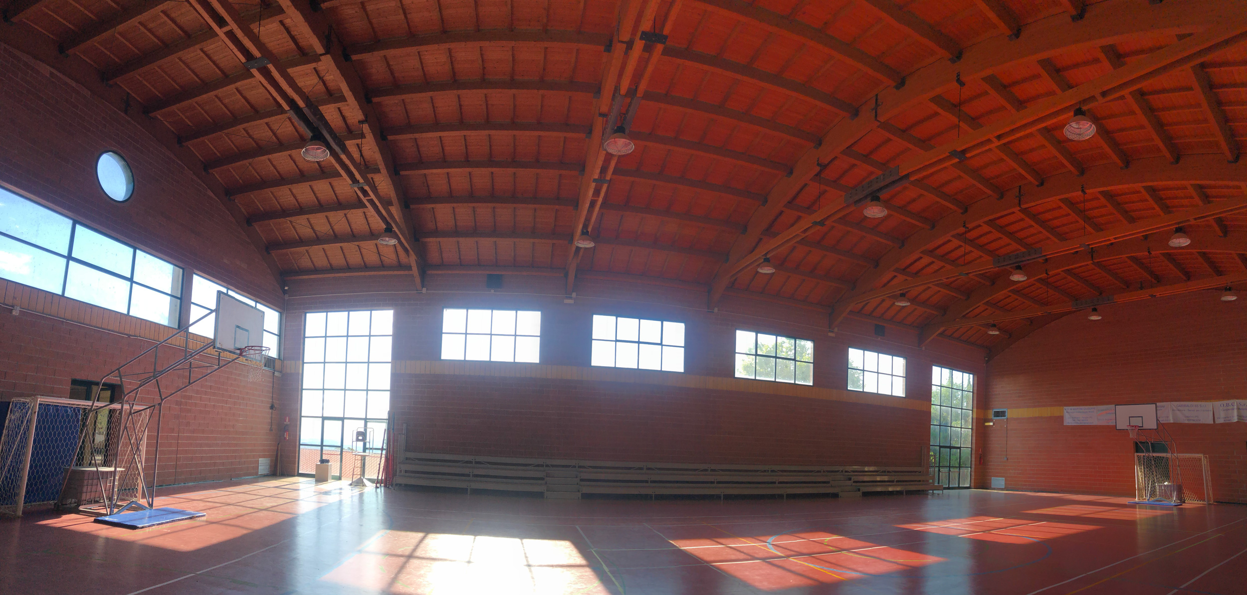 Interno della palestra comunale di Chianni con campo sportivo, copertura lignea e illuminazione tecnica, mostrata nell’ambito della progettazione dell’impianto elettrico dello Studio Tecnico Casalini.