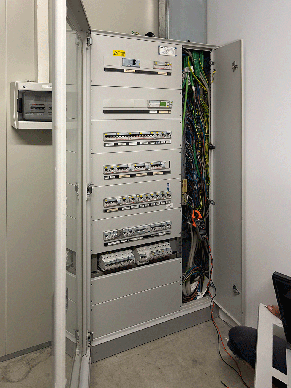 Quadro elettrico generale aperto con interruttori magnetotermici e cablaggio interno visibile.