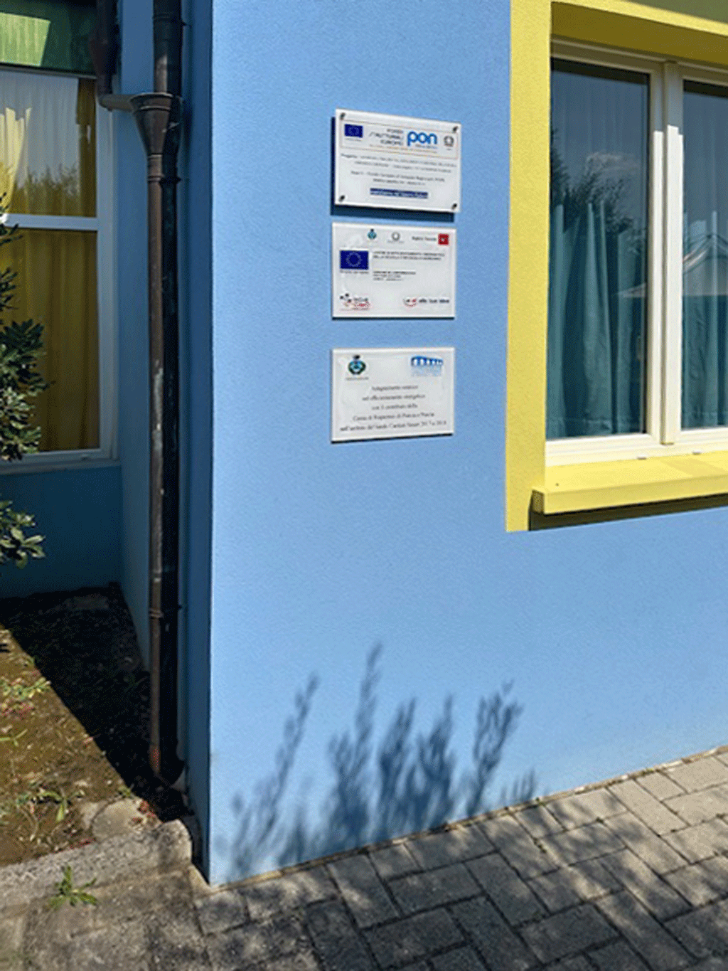 Primo piano di targhe informative PON ed efficientamento energetico su muro esterno azzurro.