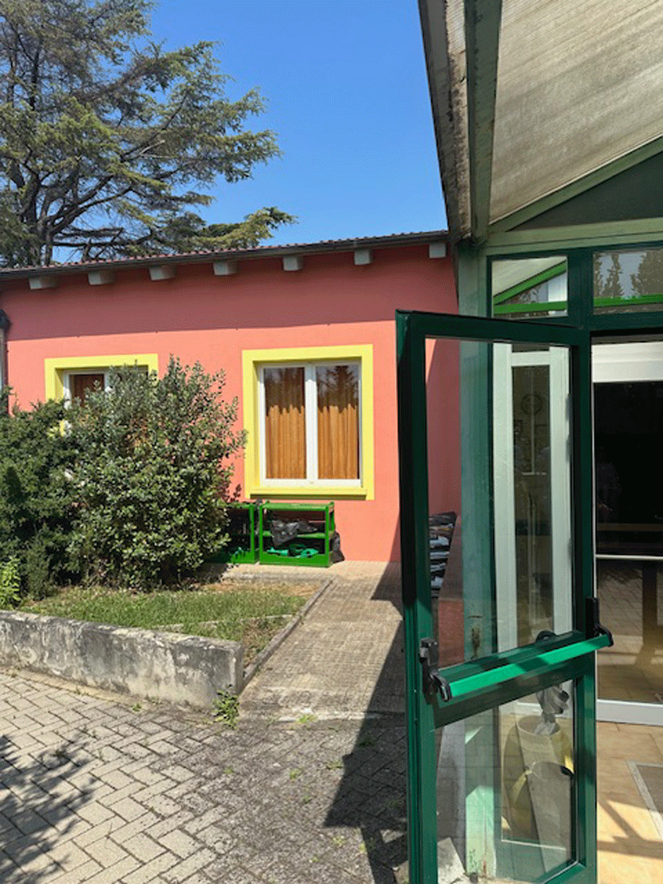 Ingresso con porta a vetri verde e vista sulla facciata arancione dell'edificio.