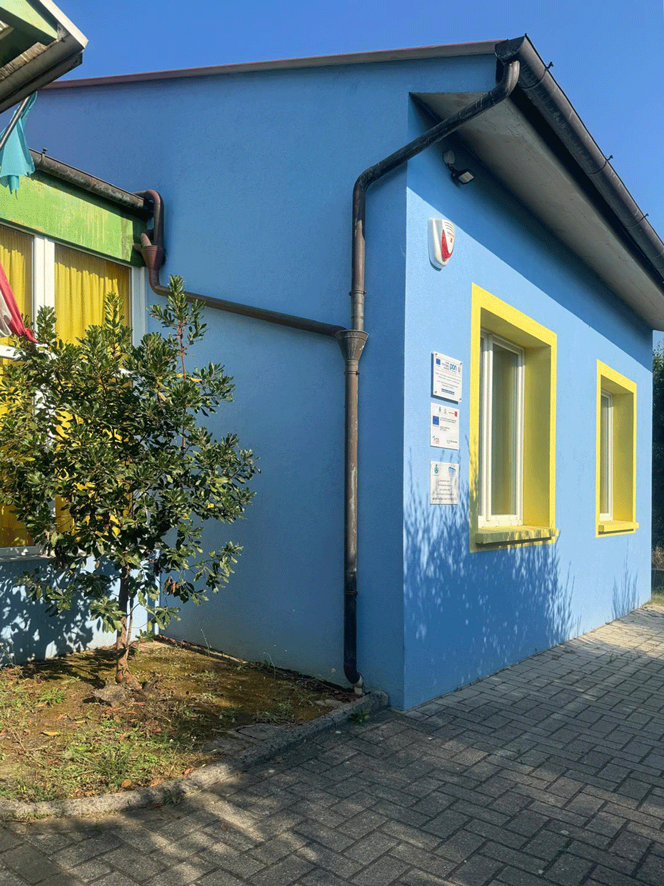 Facciata esterna azzurra con infissi gialli e pluviali di un edificio pubblico a Lamporecchio.