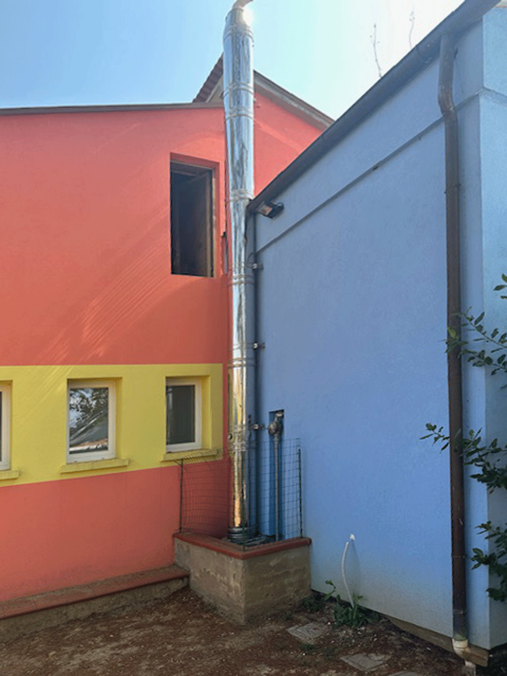 Canna fumaria esterna in acciaio installata tra due pareti colorate di un edificio a Lamporecchio.