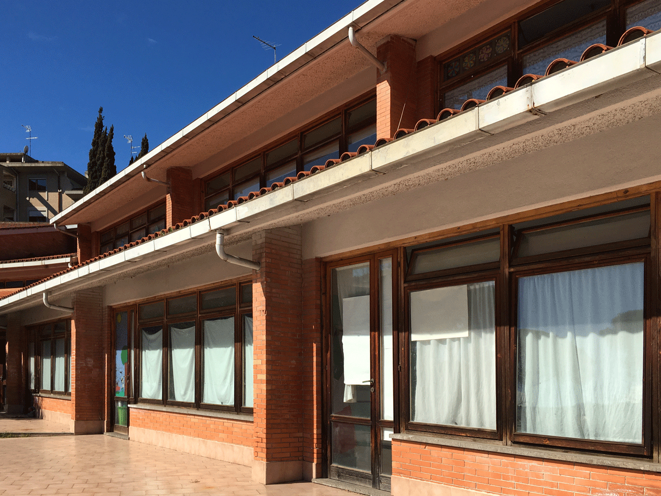 Dettaglio architettonico di una scuola con porticato, pilastri in mattoni e pluviali esterni.