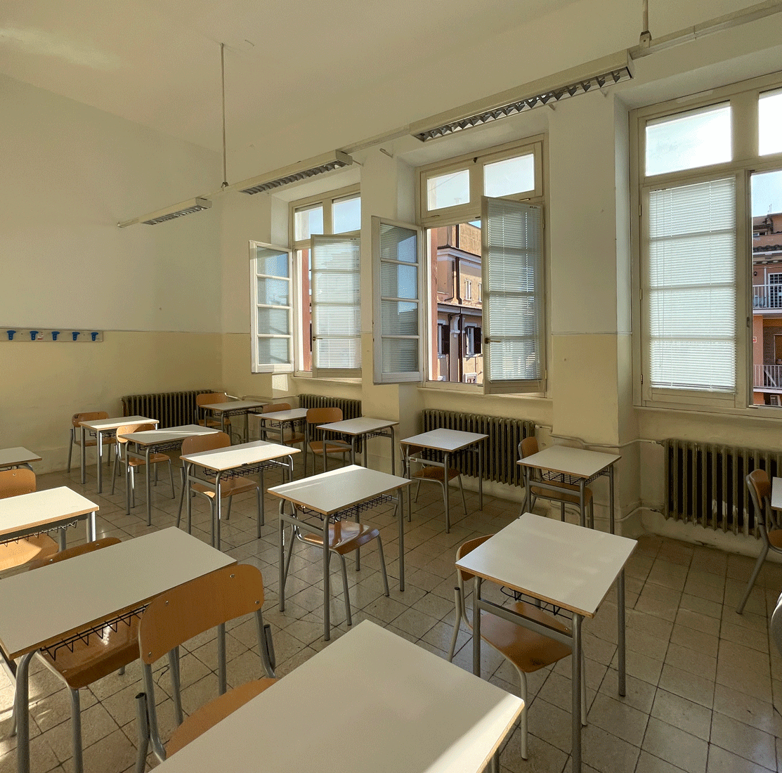 Aula scolastica vuota con banchi singoli e grandi finestre.