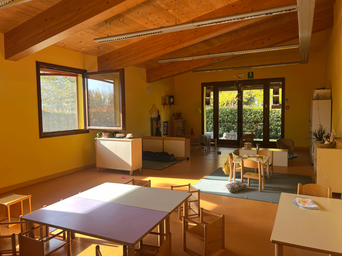 Interno dell'asilo Gatto con gli Stivali con soffitto in legno, tavoli per bambini e grande vetrata luminosa.