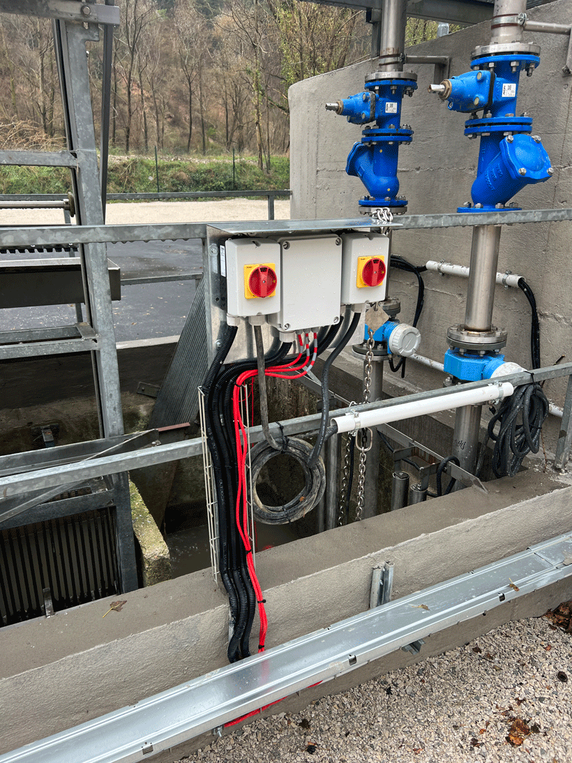 Cablaggi elettrici con guaine flessibili e sezionatori d'emergenza installati su tubazioni idrauliche industriali.
