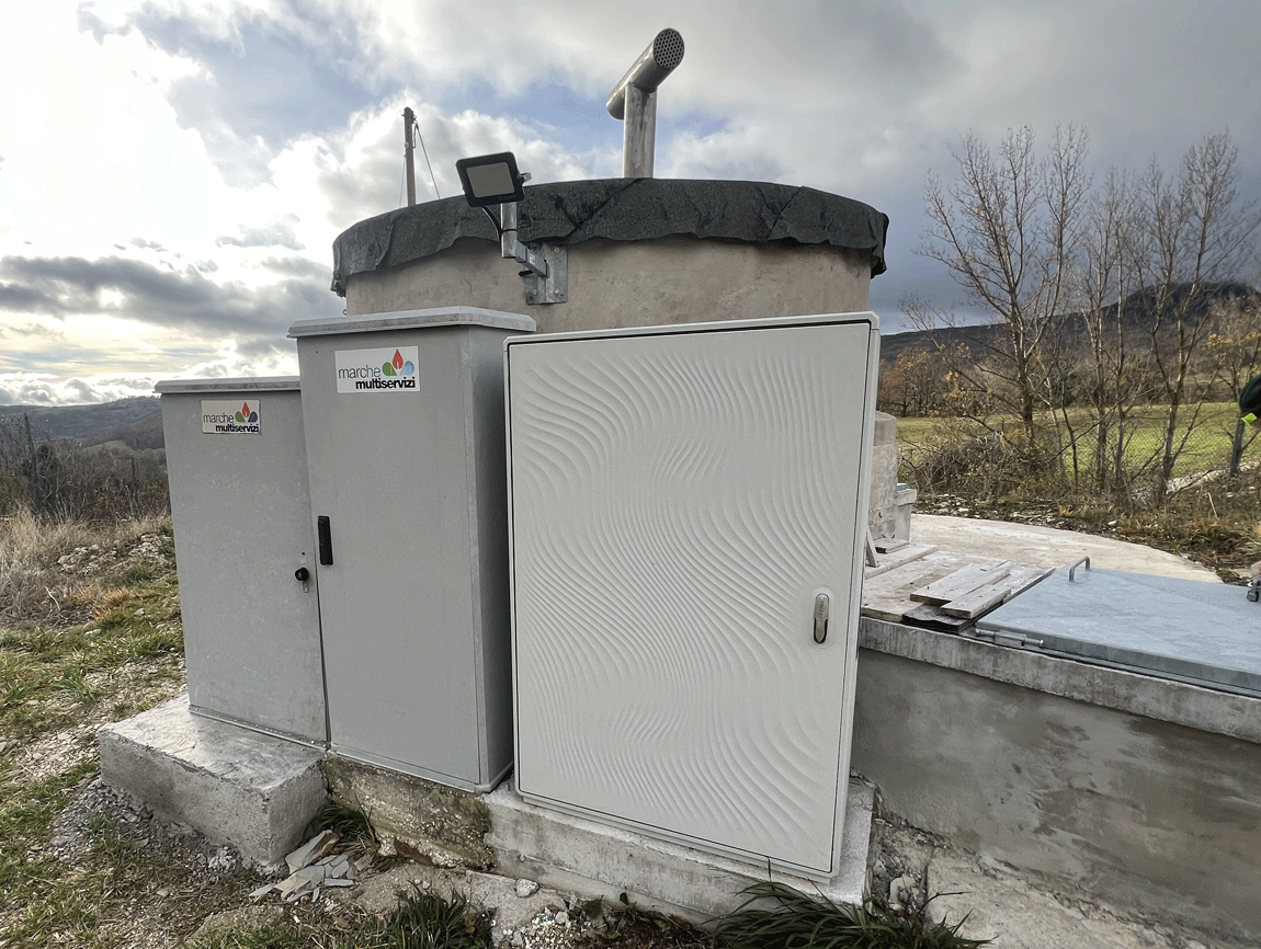 Quadri elettrici stradali con logo Marche Multiservizi installati accanto a un manufatto in cemento di un impianto idrico.