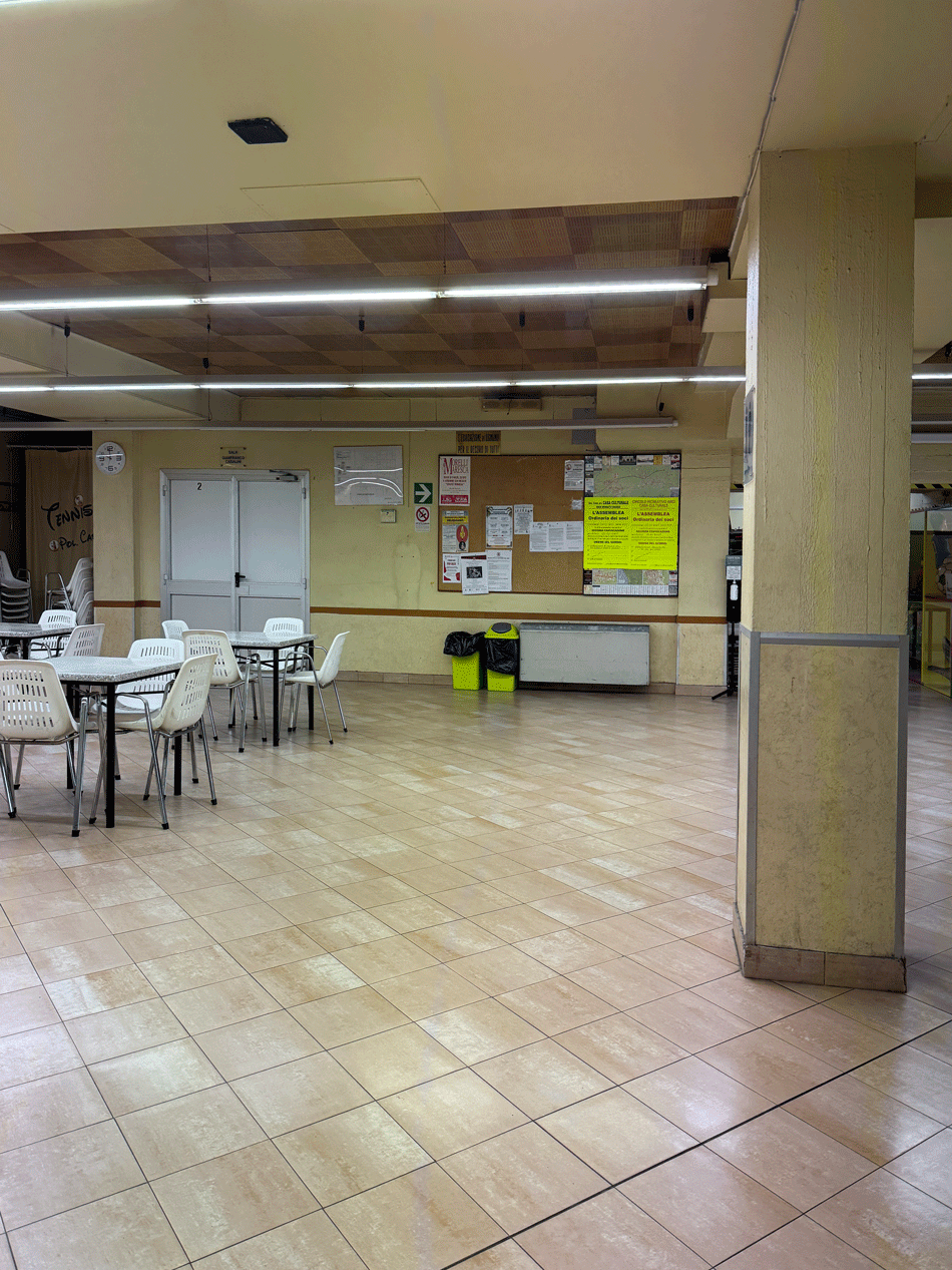 Sala conferenze e ricreativa, con tavoli, bacheca informativa e terminali dell'impianto di riscaldamento a parete.