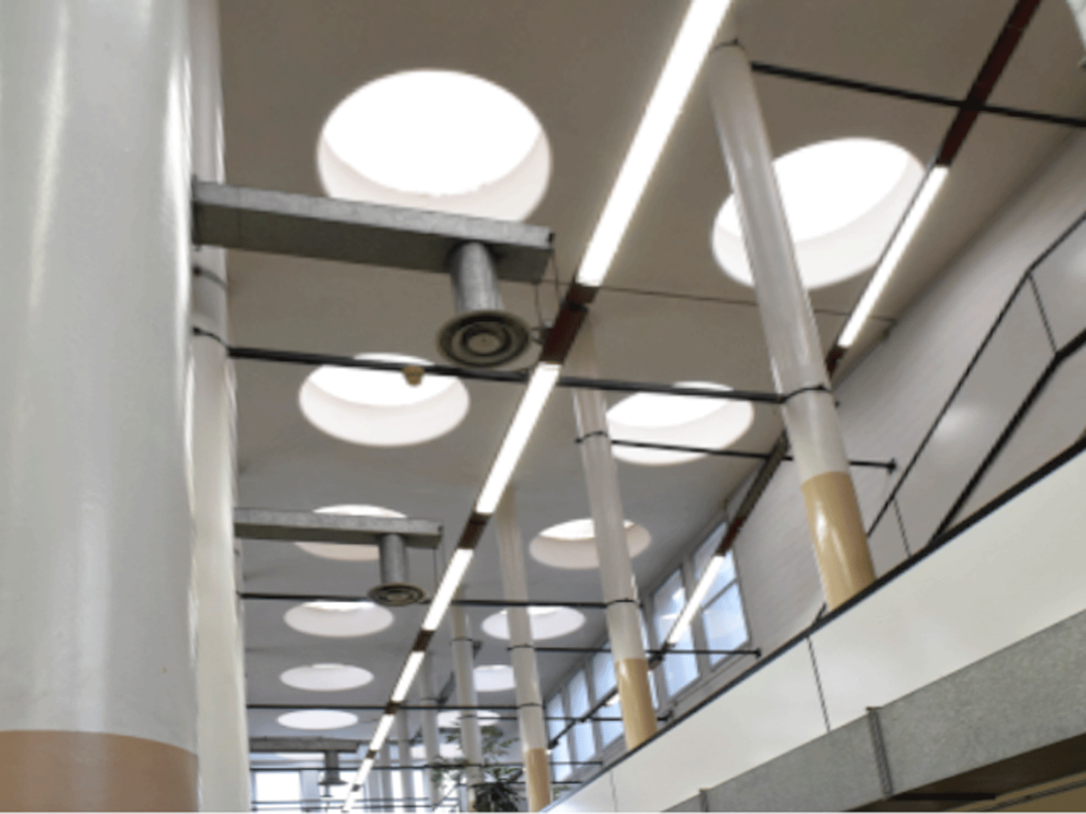 Soffitto architettonico con lucernari circolari e barre luminose sospese.