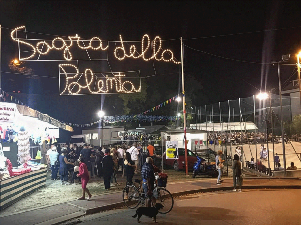 Ingresso notturno della Sagra della Polenta a Castelfranco di Sotto con insegna luminosa, bancarelle e afflusso di pubblico.