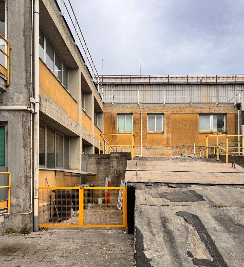 Esterno dello stabilimento Saint-Gobain di Pisa con coperture tecniche, facciate industriali e percorsi di servizio.