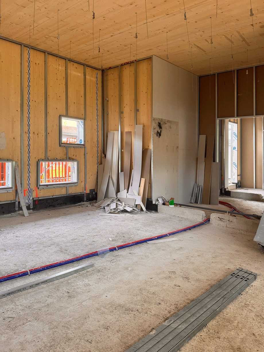 Spazio interno del cantiere con pareti in legno XLAM, sottostrutture metalliche e condutture impiantistiche.