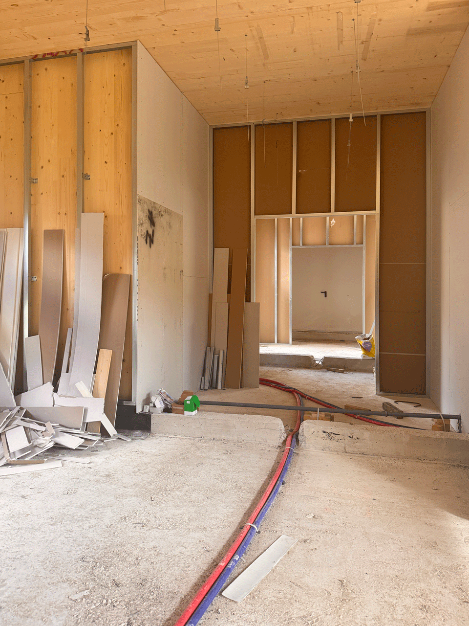 Ambiente interno del nuovo asilo nido in cantiere con solaio in legno XLAM e passaggio delle tubazioni a pavimento.