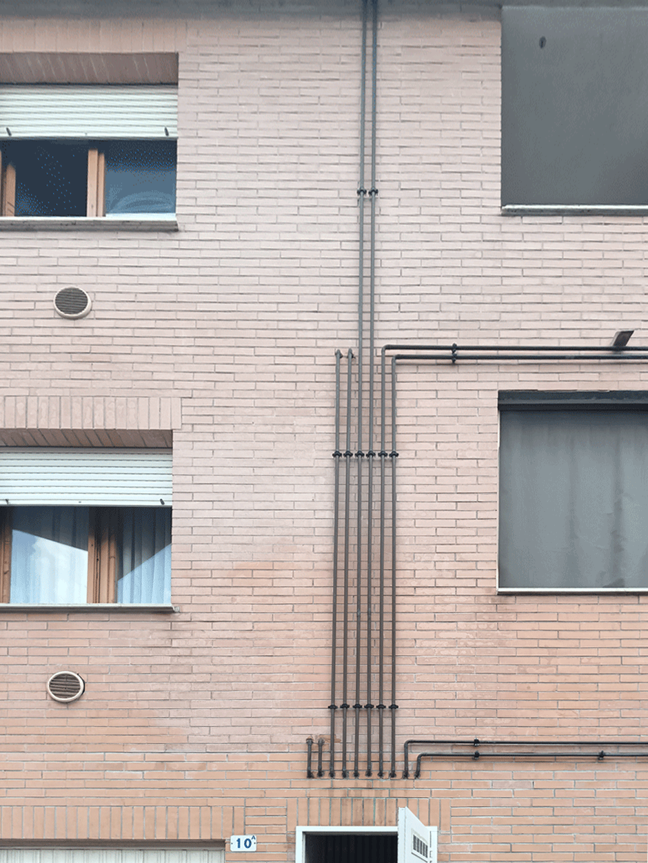 Dettaglio della facciata in laterizio con tubazioni impiantistiche esterne di un immobile Siena Casa.